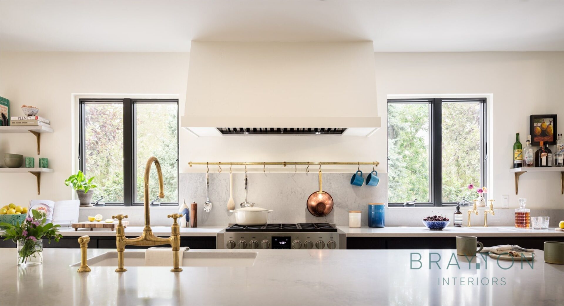 A custom drywall range hood anchors the feature wall of the kitchen. Antique brass faucets and utensil rail are the perfect accent pieces that won't go out of style.